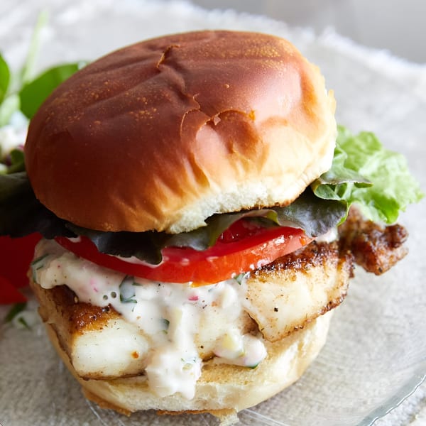 Close-up of a fish sandwich on a brioche bun with lettuce, tomato, and tartar sauce.