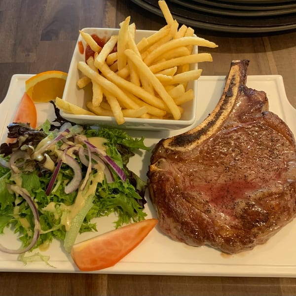 A French bistro meal with a large bone-in steak, a side salad, and a bowl of french fries.