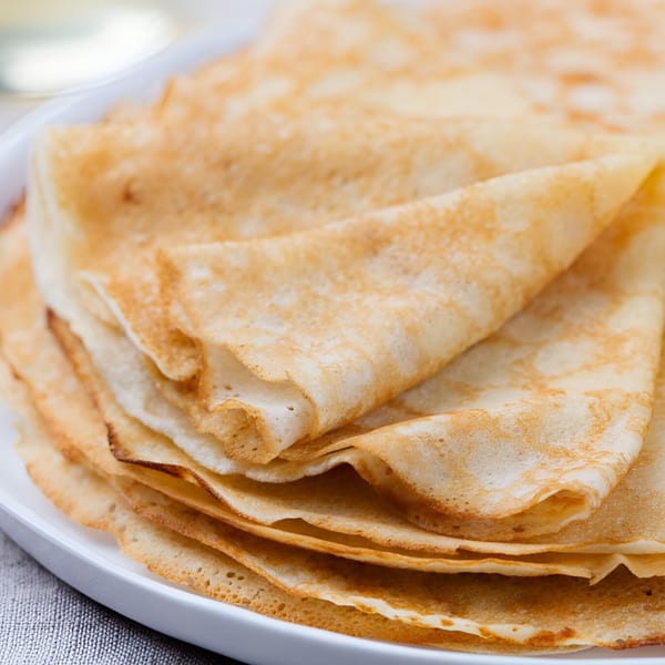 A stack of golden-brown French crepes, folded and layered on a white plate.