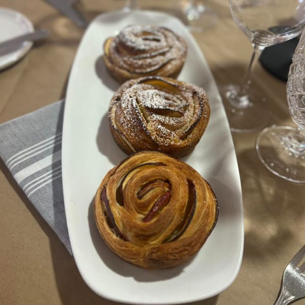 Three golden-brown French pastries, two dusted with powdered sugar, on a white rectangular plate.