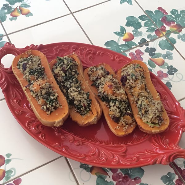 Four butternut squash halves, stuffed with a grain and herb mixture, on a red serving platter.