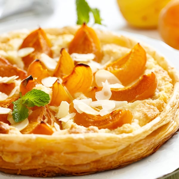 Golden apricot tart with sliced almonds and a mint garnish on a white plate.