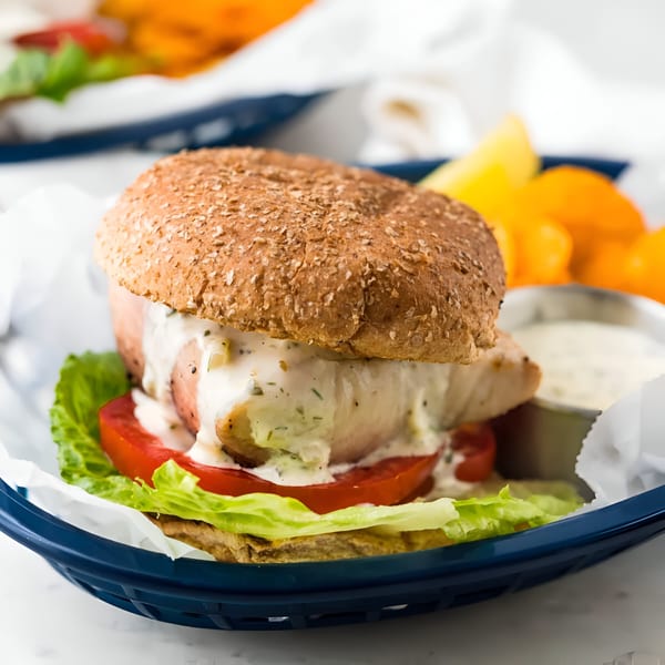 Chicken sandwich with lettuce, tomato, and creamy sauce in a blue basket with fries and dip.